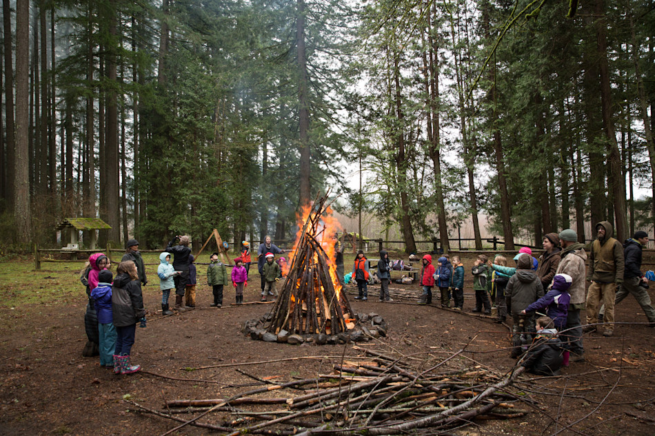 A circle of bundled-up kids and Guides gathered around a tall winter bonfire in the forest