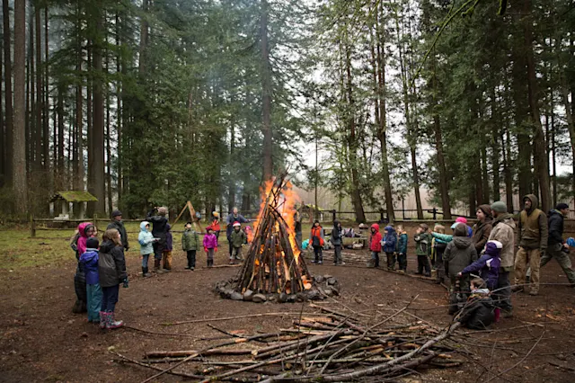 A circle of bundled-up kids and Guides gathered around a tall winter bonfire