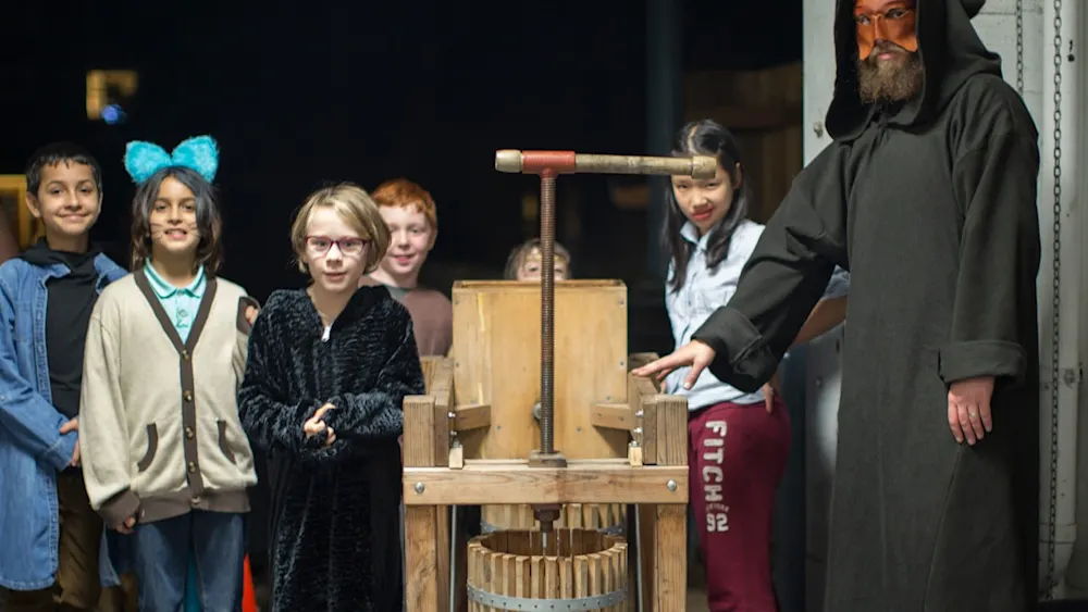 Kids at a cider press with a hooded figure at Track-or-Treat