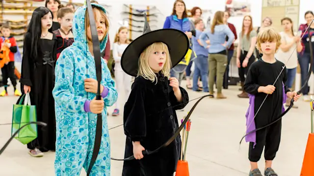 Kids in Halloween costumes with bows at the archery range