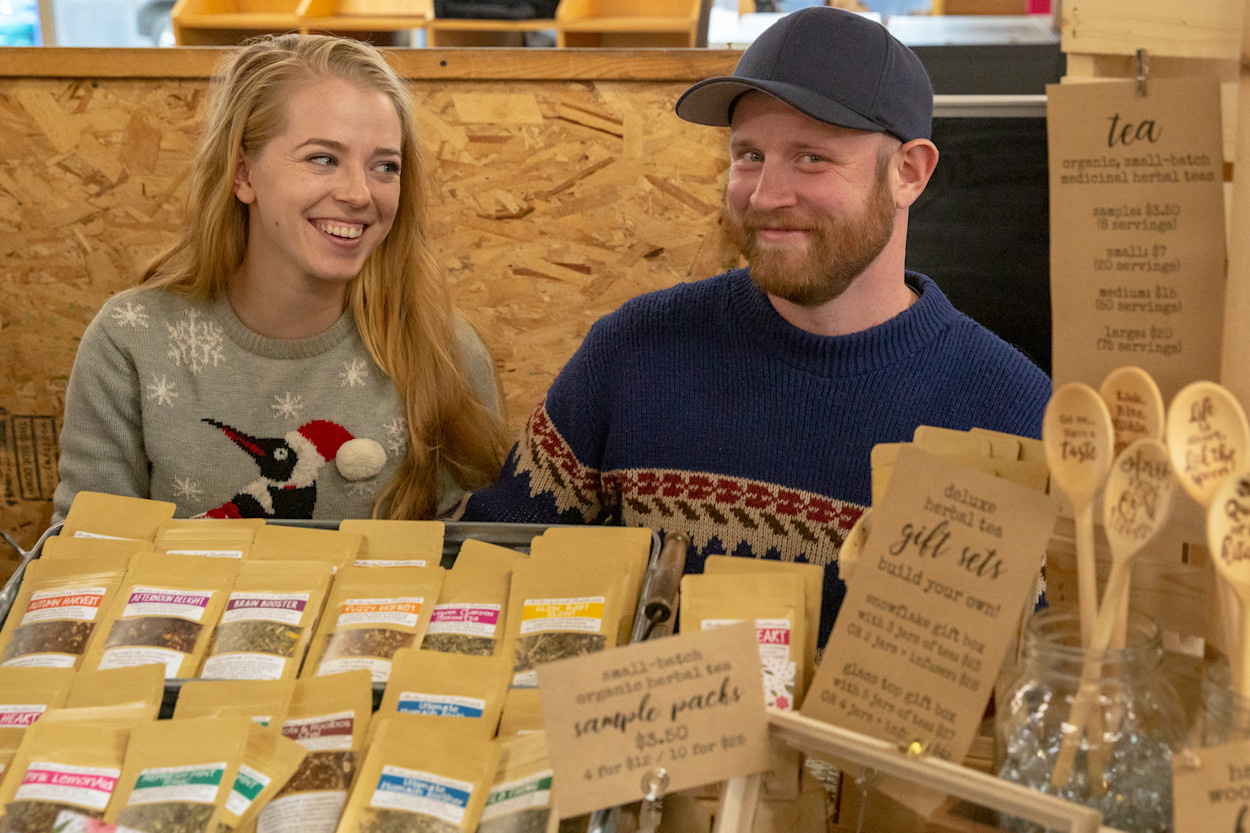 Two grown-ups in holiday sweaters grinning at a craft table