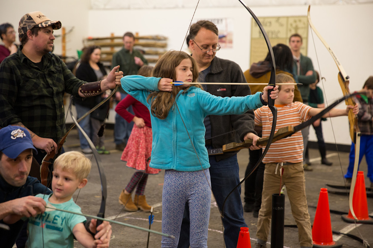 Families drawing bows on the archery range at the Holiday Faire