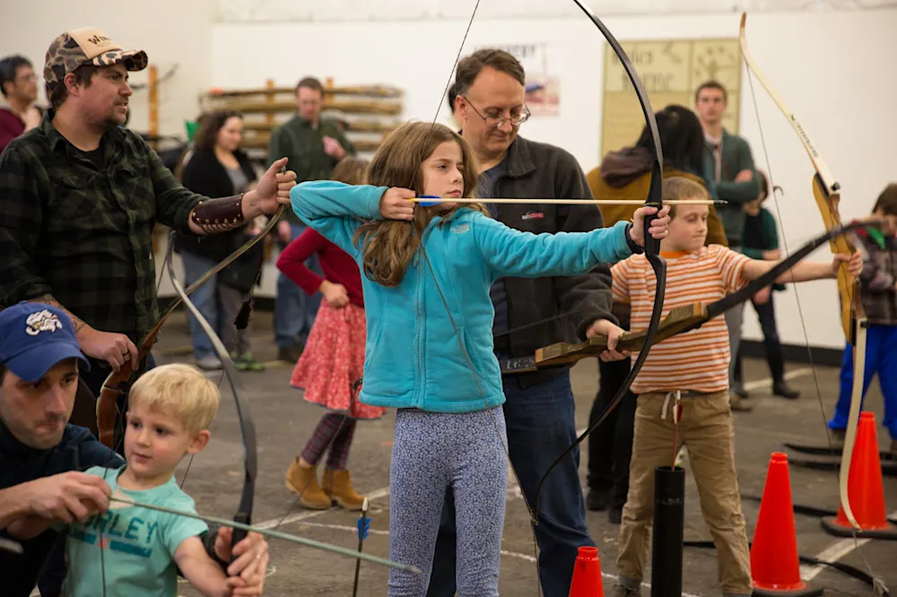 Families drawing bows on the archery range at the Holiday Faire