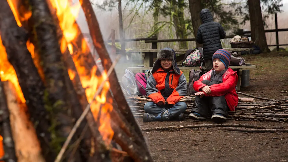 Two bundled-up kids sitting beside a tall winter bonfire